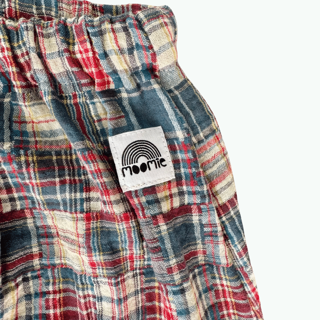 Gros plan sur le tissu en gaze de coton à carreaux et l'étiquette Moomie du pantalon bébé fabriqué en France.