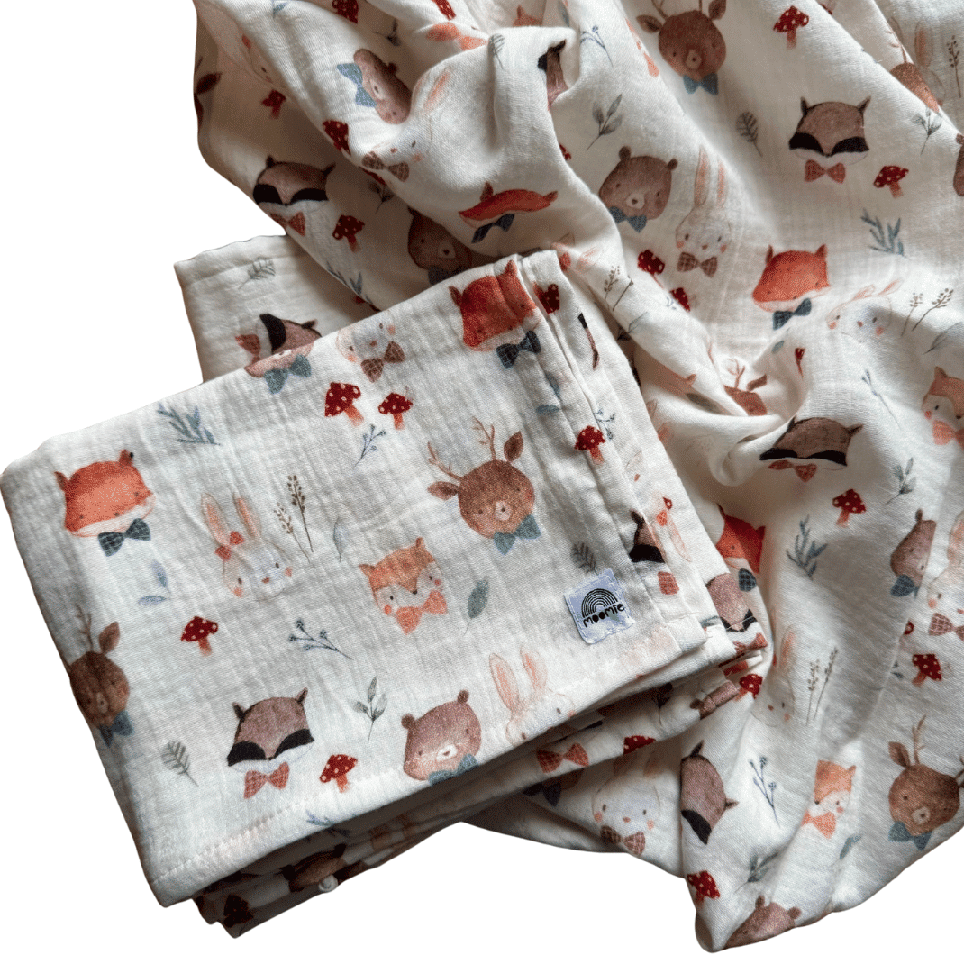 Lange bébé en coton doux avec imprimé animaux de la forêt, plié avec tissu déployé en arrière-plan