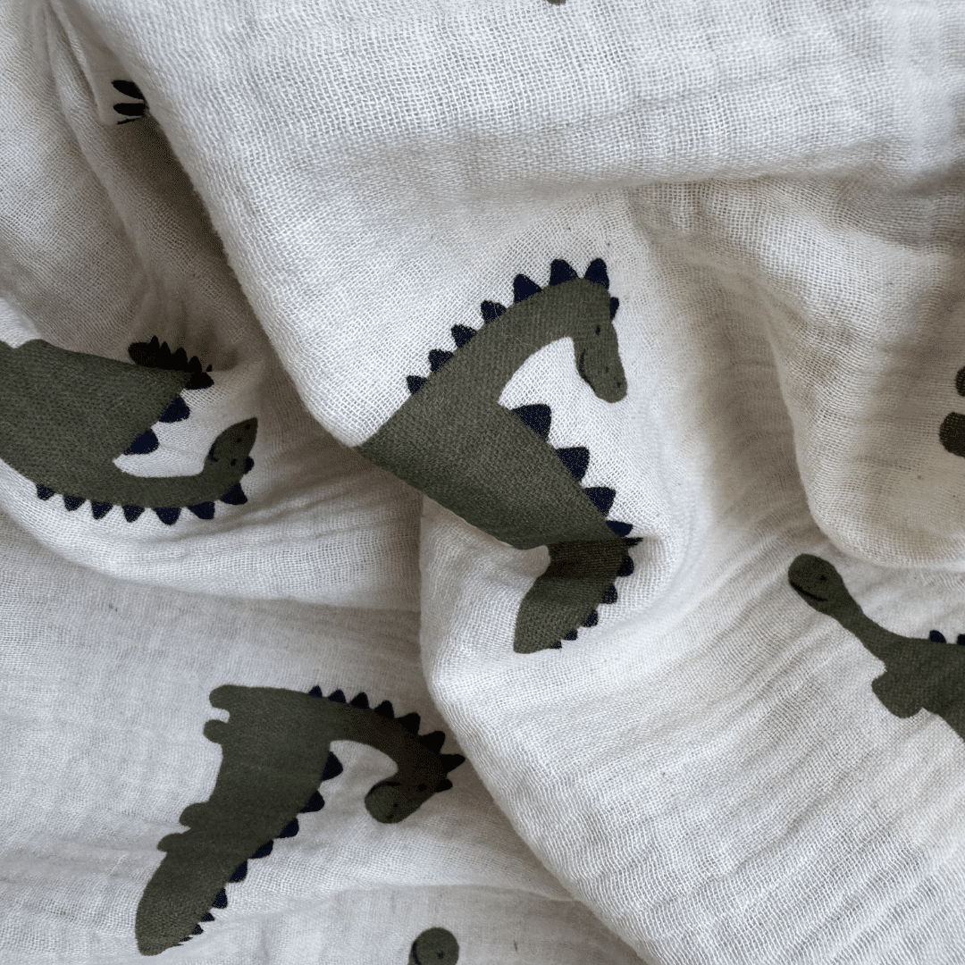 Gros plan sur l'imprimé dinosaure kaki et bleu marine du lange bébé en gaze de coton bio GOTS