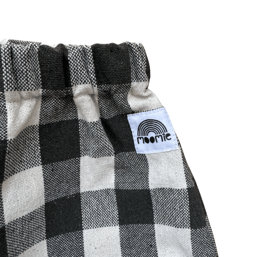 Détail de l'étiquette Moomie cousue sur un pantalon bébé à carreaux kaki et écru