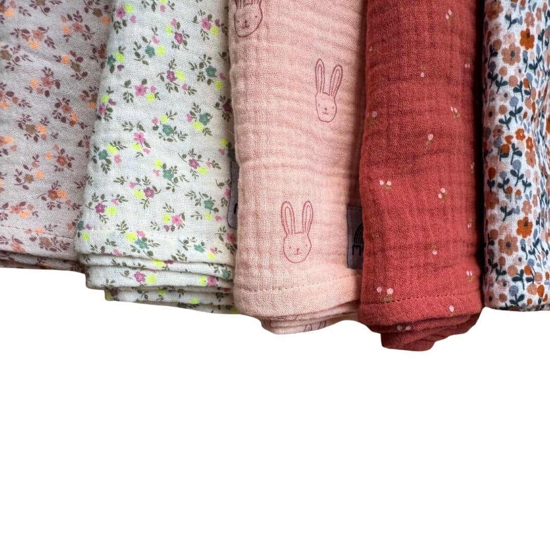 Détail des langes bébé en gaze de coton aux motifs fleuris, lapins et tons terracotta